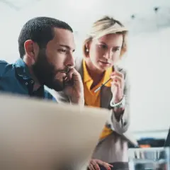 Dwóch współpracowników analizuje dane na laptopie, zastanawiając się, od jakiej kwoty opłaca się b2b.