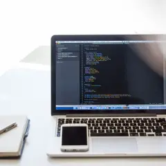 Laptop z kodem, notatnik i smartfon. Praca zdalna, usługi związane z tworzeniem stron internetowych, kodowaniem i projektowaniem, klasyfikowane jako pkwiu 62.01.1.