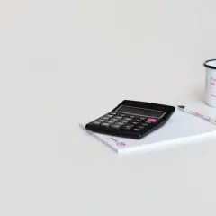 Kalkulator, notatnik i kubek z napisem "Pracuj tak, jak myślisz". Może to symbolizuje cel 6k brutto?