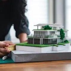 Architektka precyzyjnie mierzy model domu, zastanawiając się, ile zarabia architekt w Polsce.