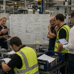 Zespół analizuje dane produkcyjne, omawiając chronometraż pracy i wskaźniki KPI przy tablicy.