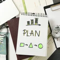 Plan rozwoju pracownika: wykresy, notatnik z napisem "PLAN", zegarek i laptop.