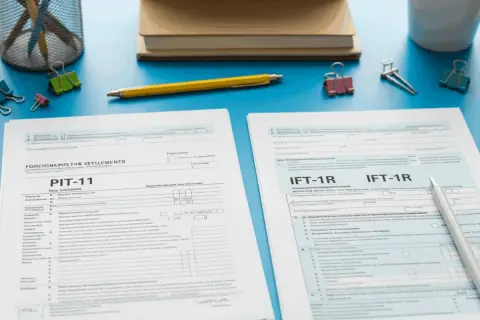 Rozliczenie obcokrajowca w Polsce: PIT-11 i formularze IFT-1R leżą na biurku obok przyborów biurowych.