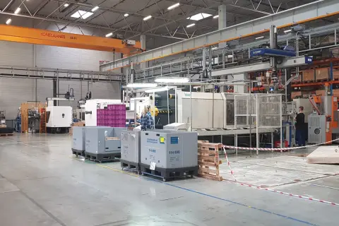 W hali produkcyjnej, podczas dni bezpieczeństwa, pracownicy nadzorują maszyny. W tle widoczny jest suwnica.