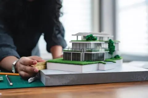 Architektka precyzyjnie mierzy model domu, zastanawiając się, ile zarabia architekt w Polsce.