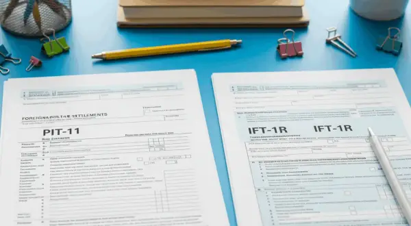 Rozliczenie obcokrajowca w Polsce: PIT-11 i formularze IFT-1R leżą na biurku obok przyborów biurowych.
