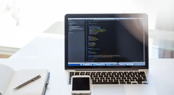 Laptop z kodem, notatnik i smartfon. Praca zdalna, usługi związane z tworzeniem stron internetowych, kodowaniem i projektowaniem, klasyfikowane jako pkwiu 62.01.1.