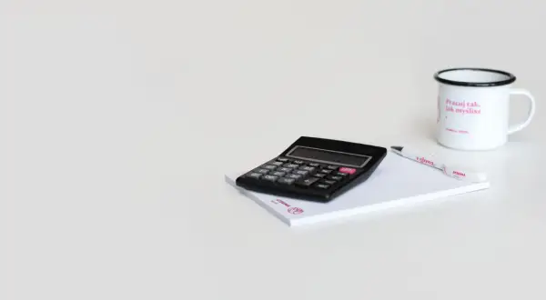 Kalkulator, notatnik i kubek z napisem "Pracuj tak, jak myślisz". Może to symbolizuje cel 6k brutto?