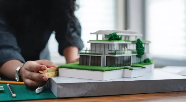 Architektka precyzyjnie mierzy model domu, zastanawiając się, ile zarabia architekt w Polsce.