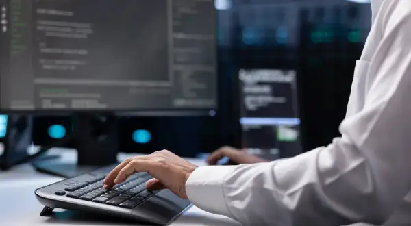 Programista w białej koszuli pracuje przy komputerze w serwerowni. Rozwój oprogramowania to kluczowy element branży usługowej.