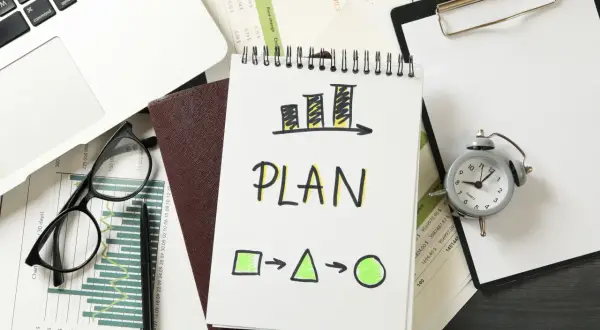 Plan rozwoju pracownika: wykresy, notatnik z napisem "PLAN", zegarek i laptop.