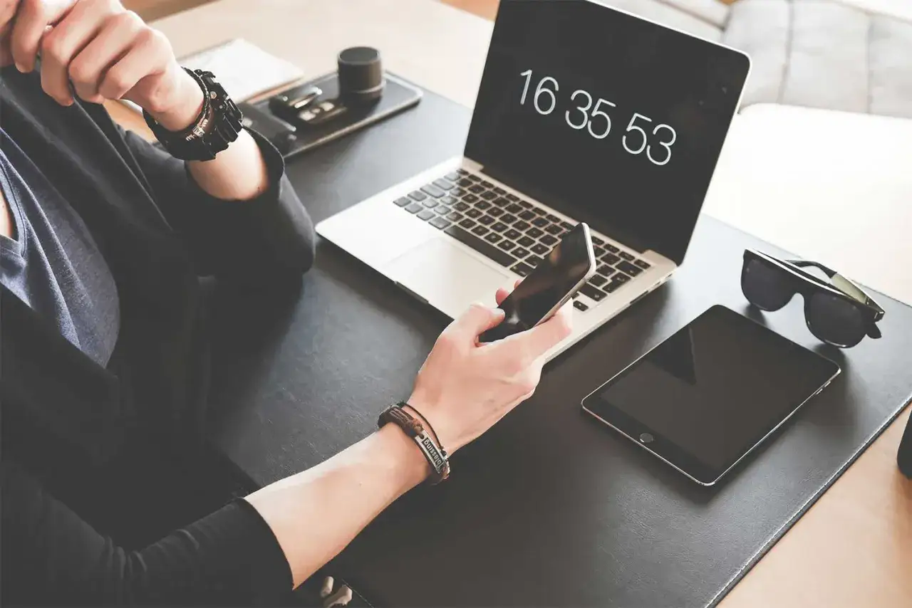 Osoba korzysta z telefonu, laptopa i tabletu, które są kluczowymi narzędziami komunikacji wewnętrznej w nowoczesnym biurze.