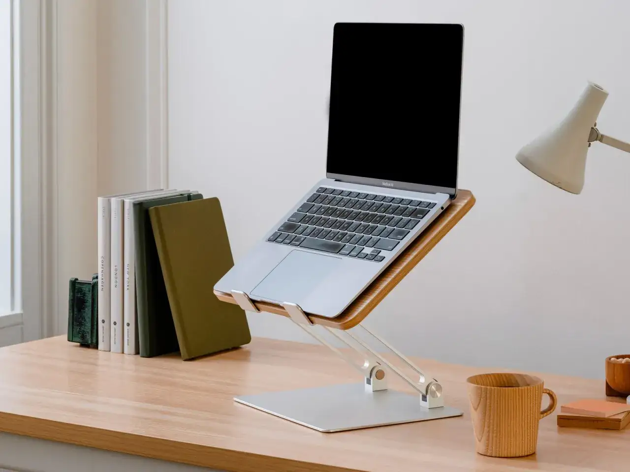 Laptop na stojaku, książki i kubek na biurku – idealne miejsce do pracy zdalnej.