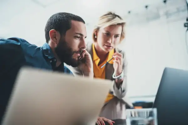 Dwóch współpracowników analizuje dane na laptopie, zastanawiając się, od jakiej kwoty opłaca się b2b.