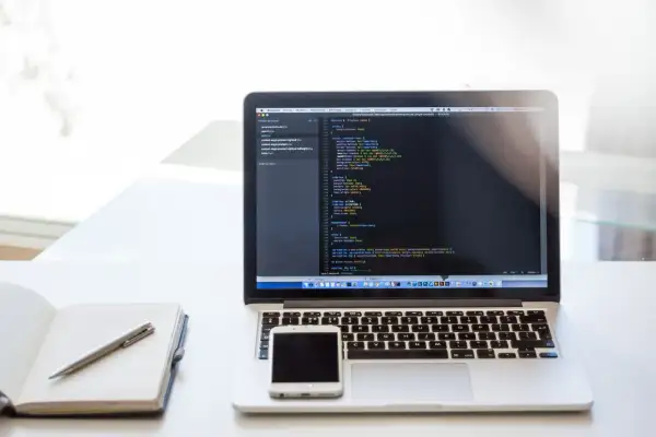Laptop z kodem, notatnik i smartfon. Praca zdalna, usługi związane z tworzeniem stron internetowych, kodowaniem i projektowaniem, klasyfikowane jako pkwiu 62.01.1.