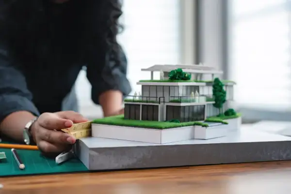 Architektka precyzyjnie mierzy model domu, zastanawiając się, ile zarabia architekt w Polsce.