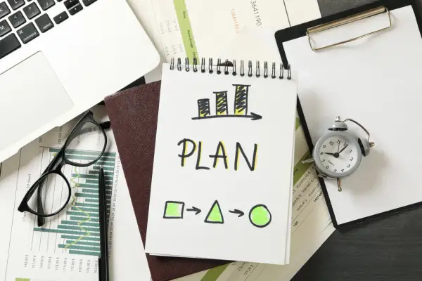 Plan rozwoju pracownika: wykresy, notatnik z napisem "PLAN", zegarek i laptop.